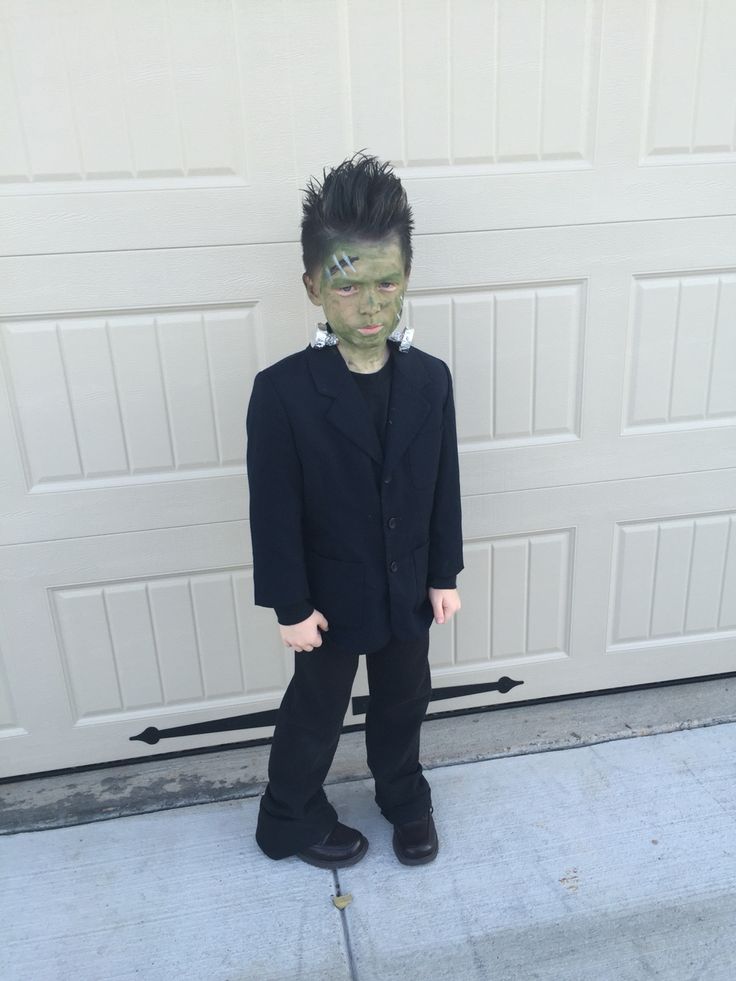 a young boy dressed up as a zombie in front of a garage door with his face painted green