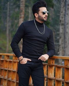 a man standing on a wooden bridge wearing sunglasses and a black turtle - neck sweater