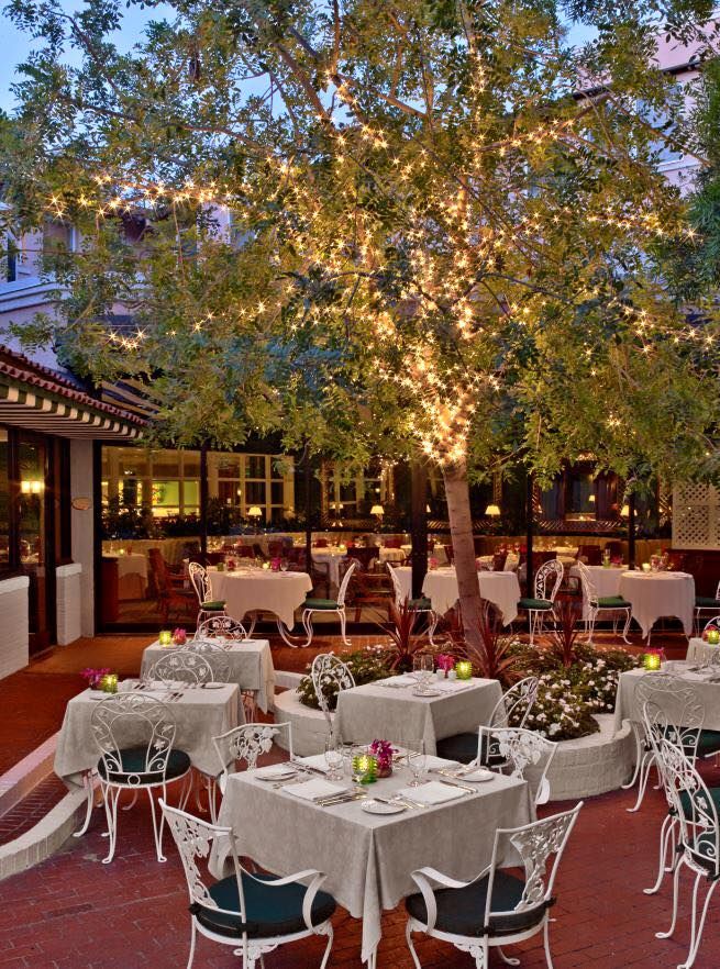 an outdoor dining area with tables, chairs and lights on the trees in the background