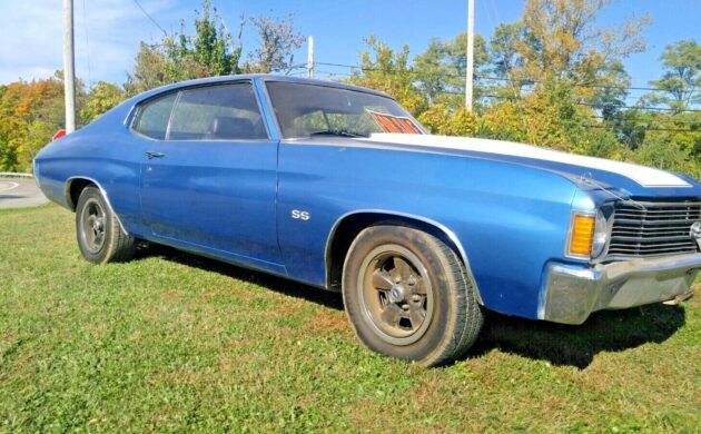 an old blue and white car is parked in the grass