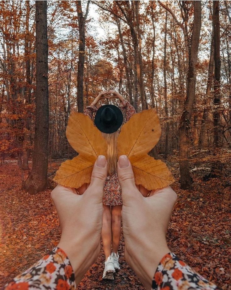 two hands holding leaves in front of a woman's face while standing in the woods