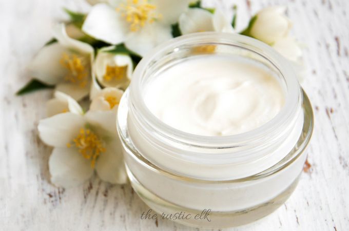 a jar of cream sitting on top of a wooden table next to white and yellow flowers