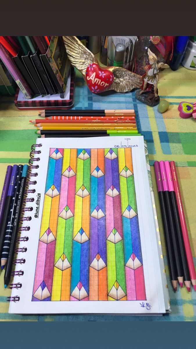 a table topped with lots of different colored pencils next to a notebook and pens