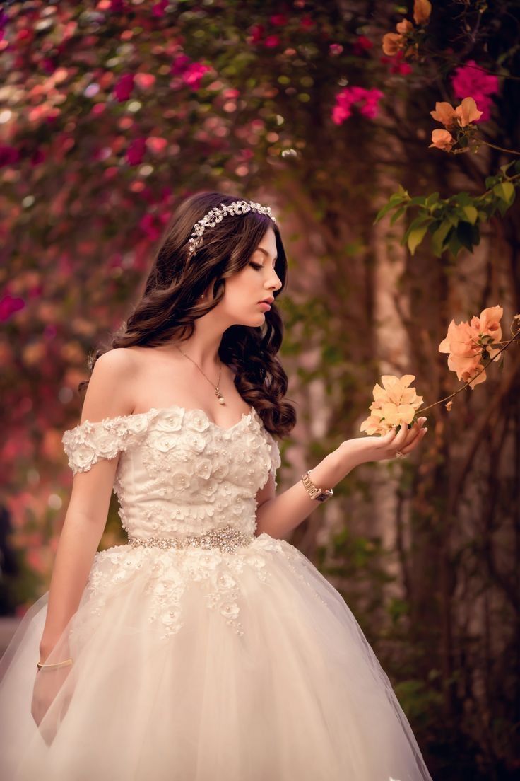 a woman in a wedding dress is holding flowers and looking at the camera while wearing a tiara