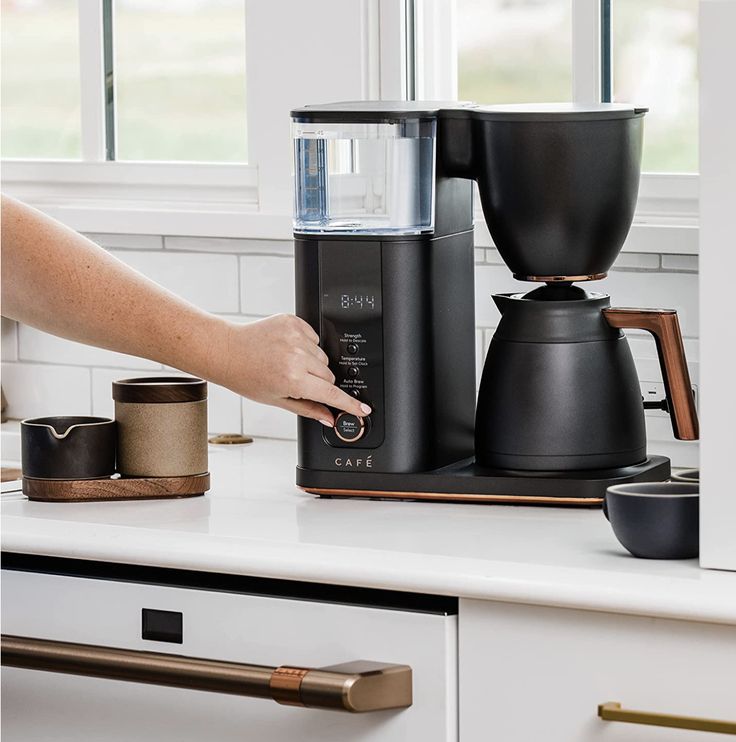 a woman's hand is pressing the button on a coffee maker in her kitchen