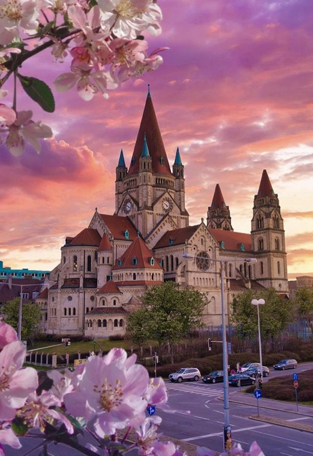 an old building with pink flowers in front of it and a purple sky behind it