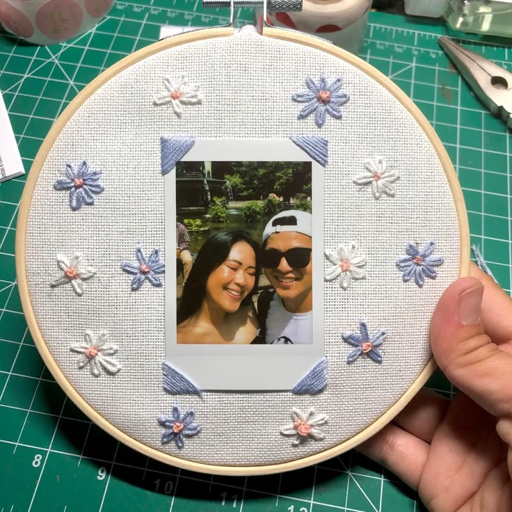 a person is holding up a photo in front of a embroidery hoop with flowers and butterflies on it