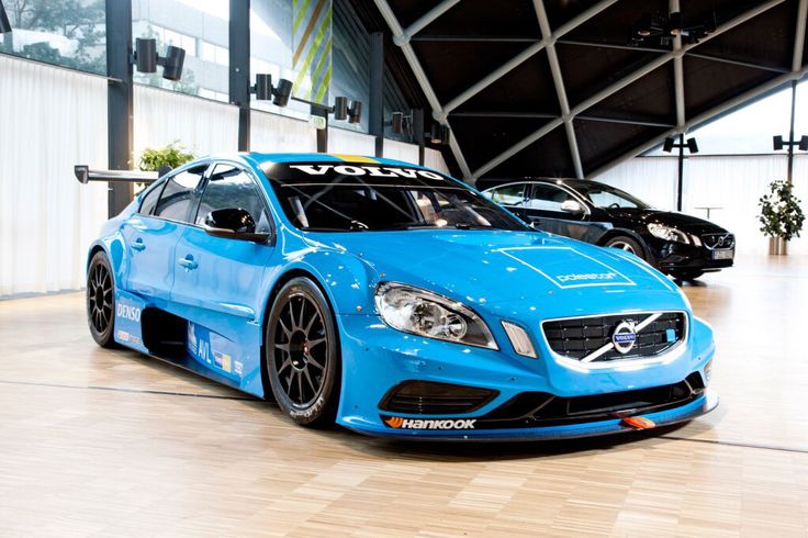 two blue sports cars parked next to each other in a room with wooden floors and large windows