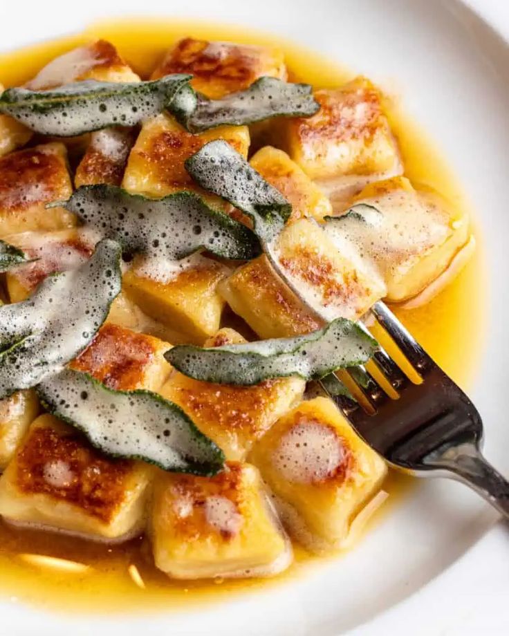 a white plate topped with ravioli covered in cheese and spinach garnish