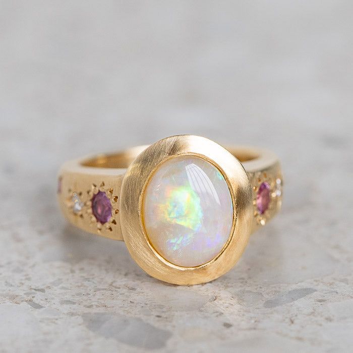 Our Sun Punch Ring has been set with a Crystal Opal from Coober Pedy and bead set with Pink Sapphires, G/VS White Diamonds and Salt & Pepper Diamonds in the band. Opal measures approx. 10 x 8mm. There are a total of three birlliant cut pink sapphires and four brilliant cut diamonds. Band width tapers from approx. 6mm to 3.4mm at the back of the band. Gold weight approx. 11g in 14ct, 12.6g in 18ct. This ring is pictured with a matte finish. For a polished finish please leave a note at the checkout. Please note, we will match the opal as close to the image as possible. Each opal is unique and may vary in appearance and colour from what is depicted on the site. Opal Inset Ring, Anthropologie Opal, Opal Wedding Ring, Coober Pedy, Crystal Opal, Bead Set, Jewelry Lookbook, Salt And Pepper Diamond, Opal Ring