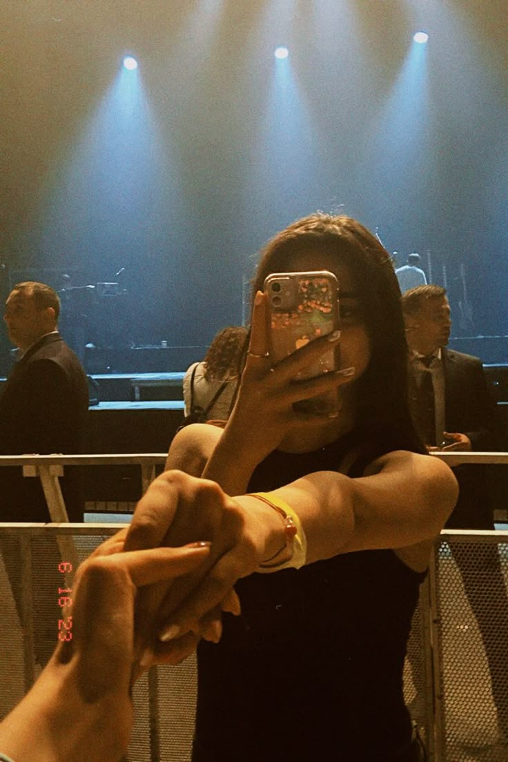 a woman taking a selfie with her cell phone in front of an audience at a concert