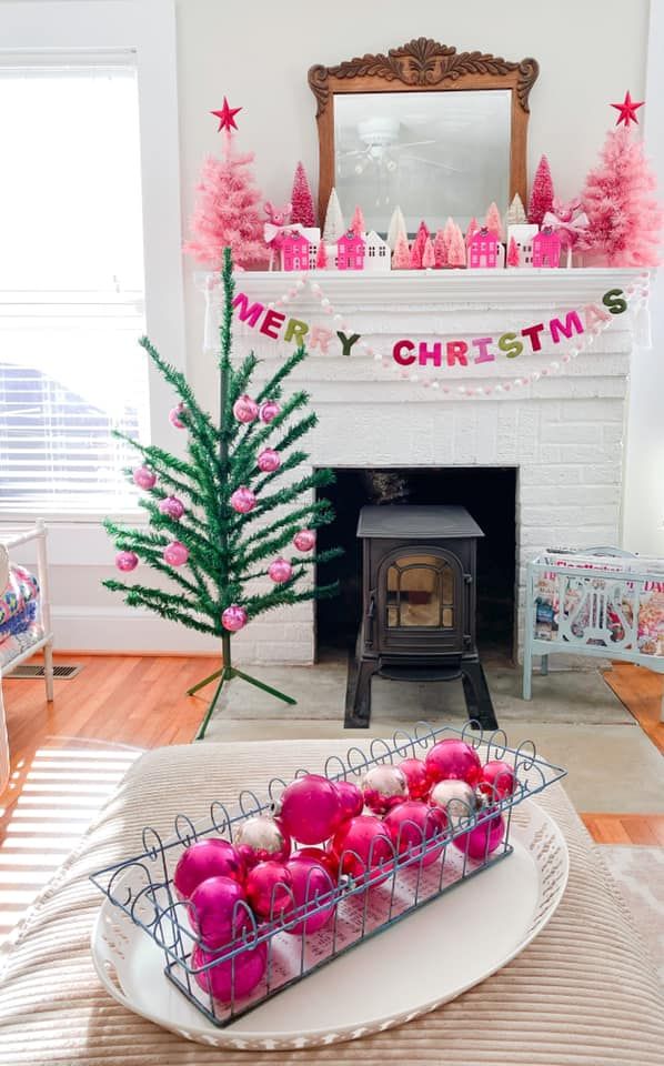 a christmas tree and fireplace in a living room with pink ornaments on the mantel