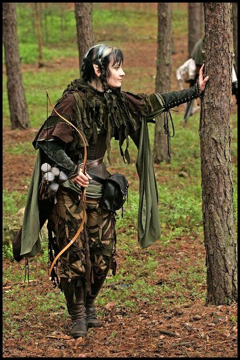 a woman dressed up as a witch holding a bird in her hand while standing next to a tree