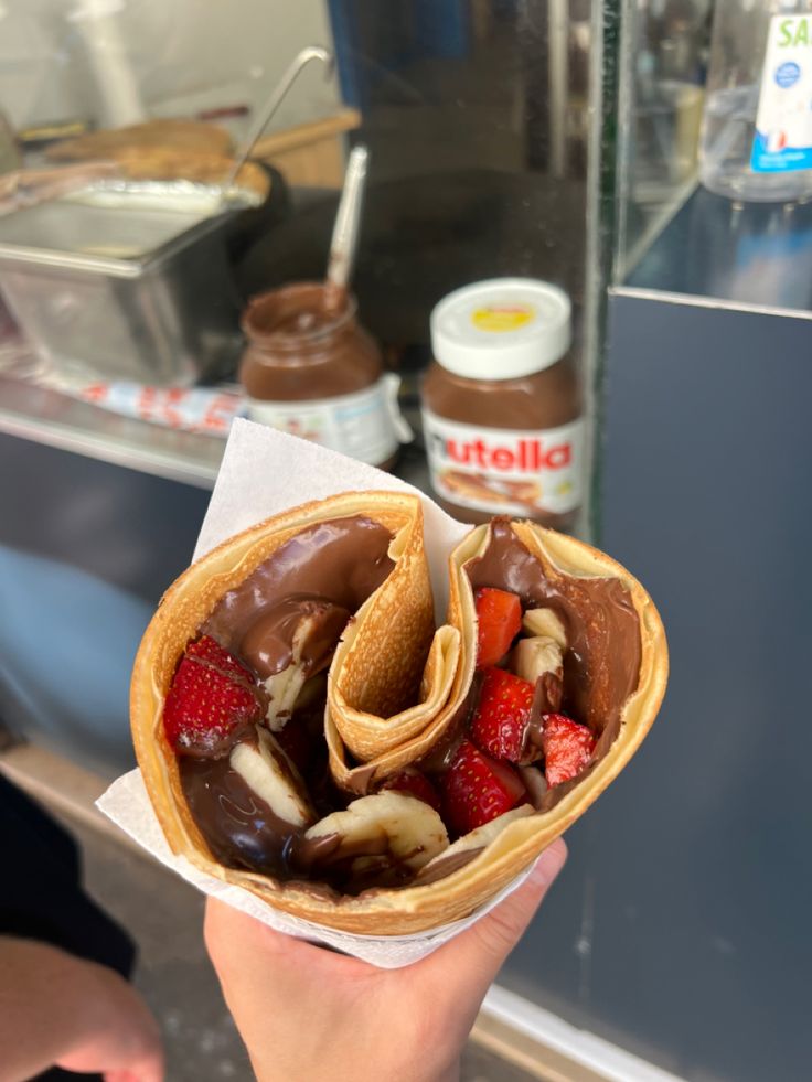 a person holding up a pastry with chocolate and strawberries in it's wrapper