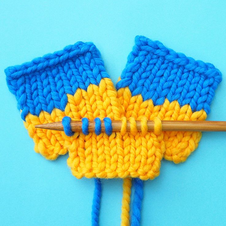 a knitted object with blue and yellow yarn on it, next to a knitting needle