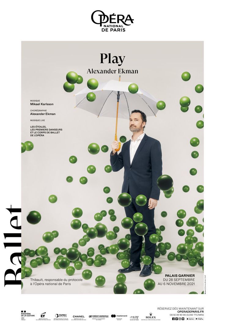 a man standing under an umbrella surrounded by green balls in front of the caption play