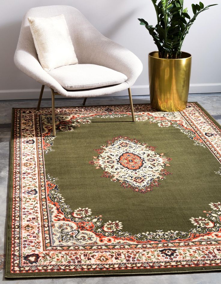 a green area rug with an ornate design on the center and side, in front of a white chair