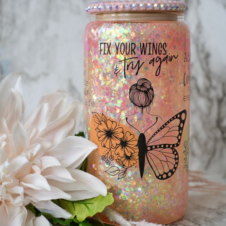 a flower and a jar with glitter on it sitting next to a white flower in front of a marble wall