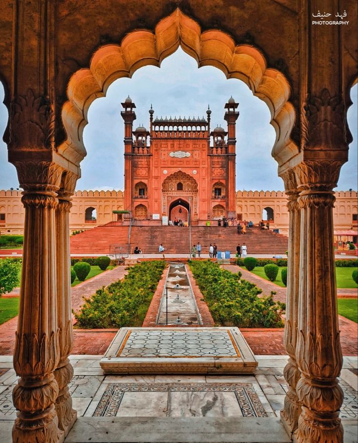 an archway leading to the red fort in india with green plants and trees on either side