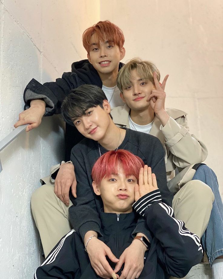 four young men sitting next to each other on top of a stair case with their hands in the air