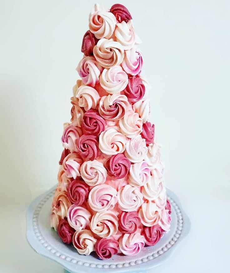 a pink and white cake with roses on it sitting on a blue plate next to a cupcake