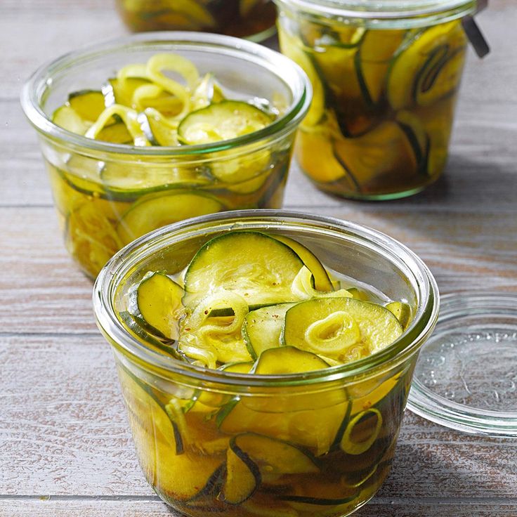 three jars filled with pickles on top of a wooden table