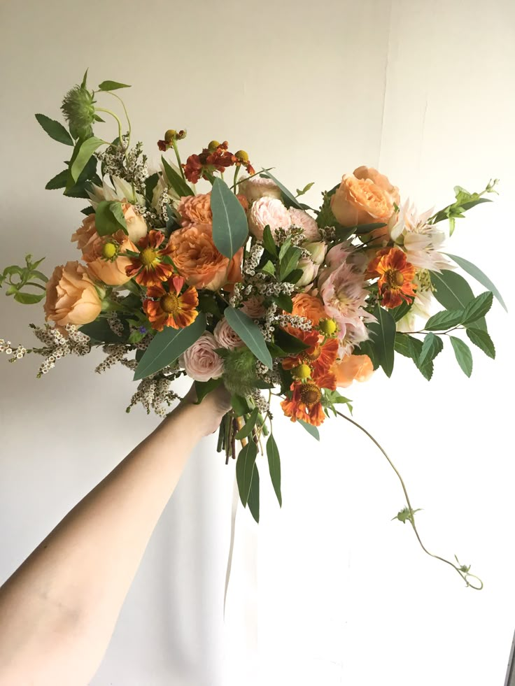 a bouquet of flowers is being held by someone's hand in front of a white wall