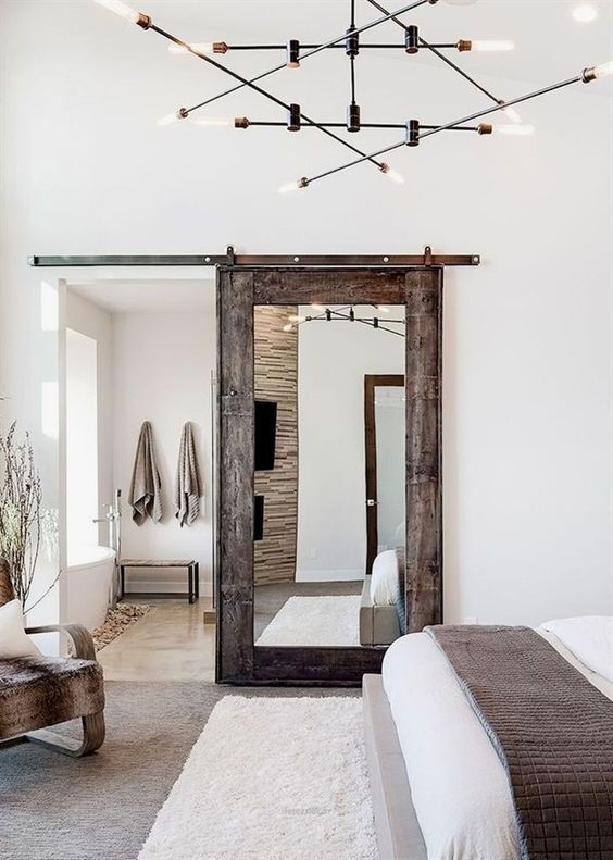 a bedroom with a bed, chair and large mirror in the room that has lights hanging from the ceiling