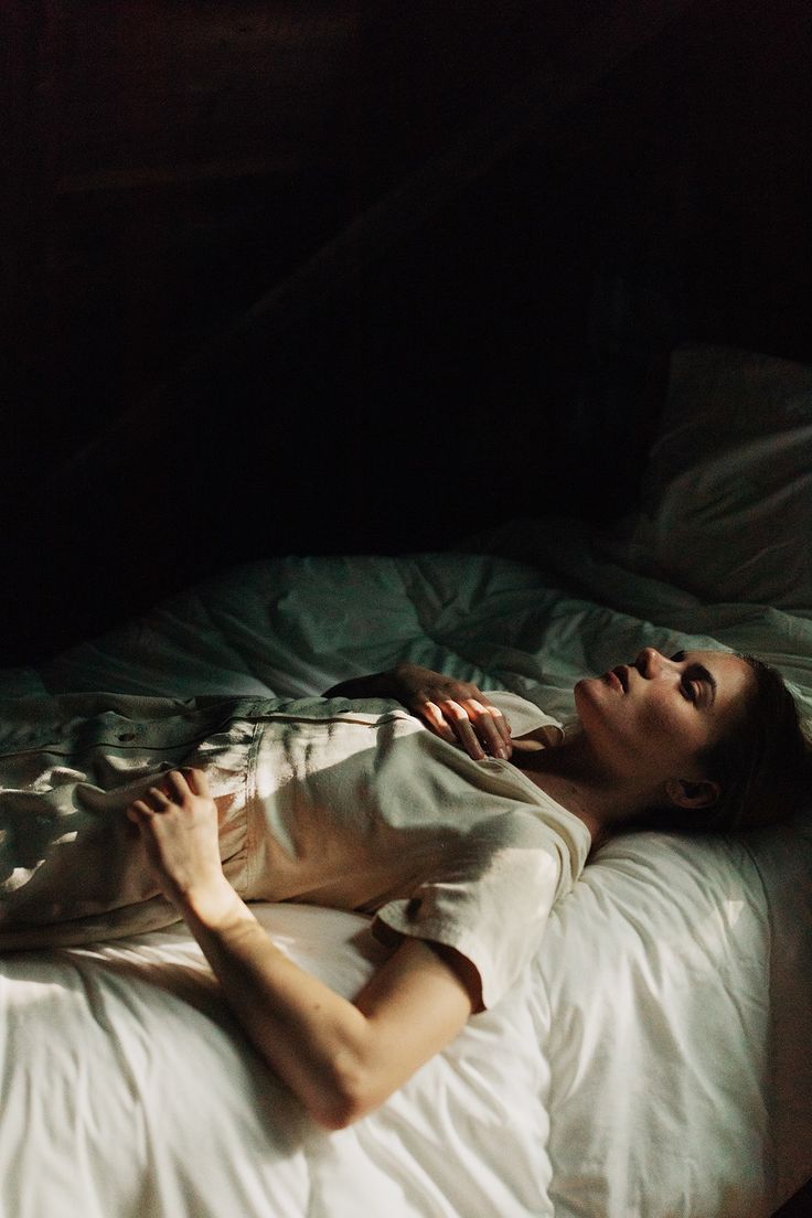 a woman laying on top of a white bed in the dark with her eyes closed