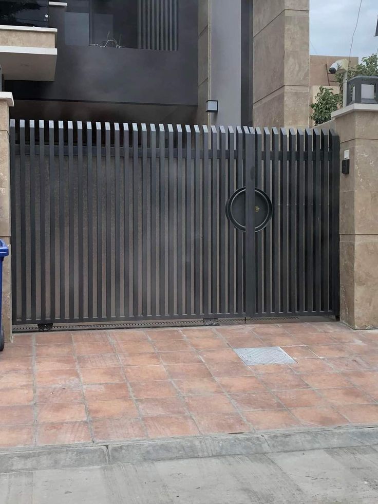 a blue trash can sitting in front of a metal fence on a sidewalk next to a building