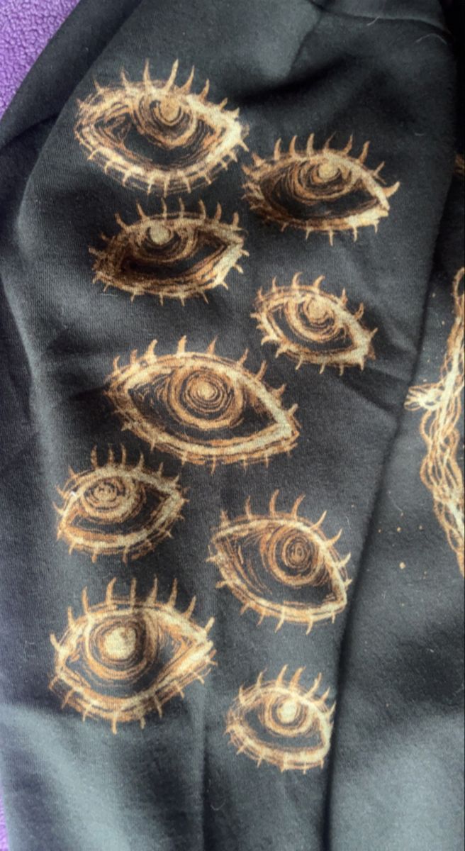 an eye scarf is laying on top of a purple blanket with black and gold designs