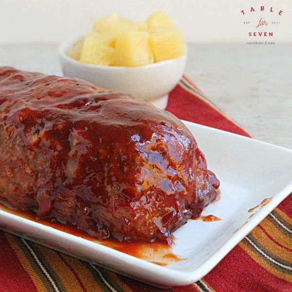 a meatloaf on a white plate next to a bowl of pineapples