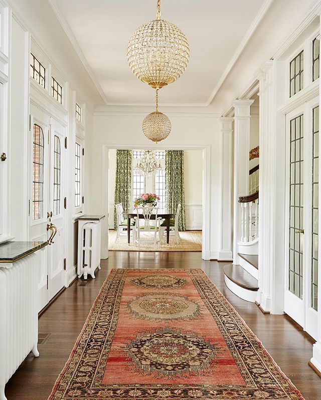 an image of a hallway with rugs and chandelier hanging from the ceiling