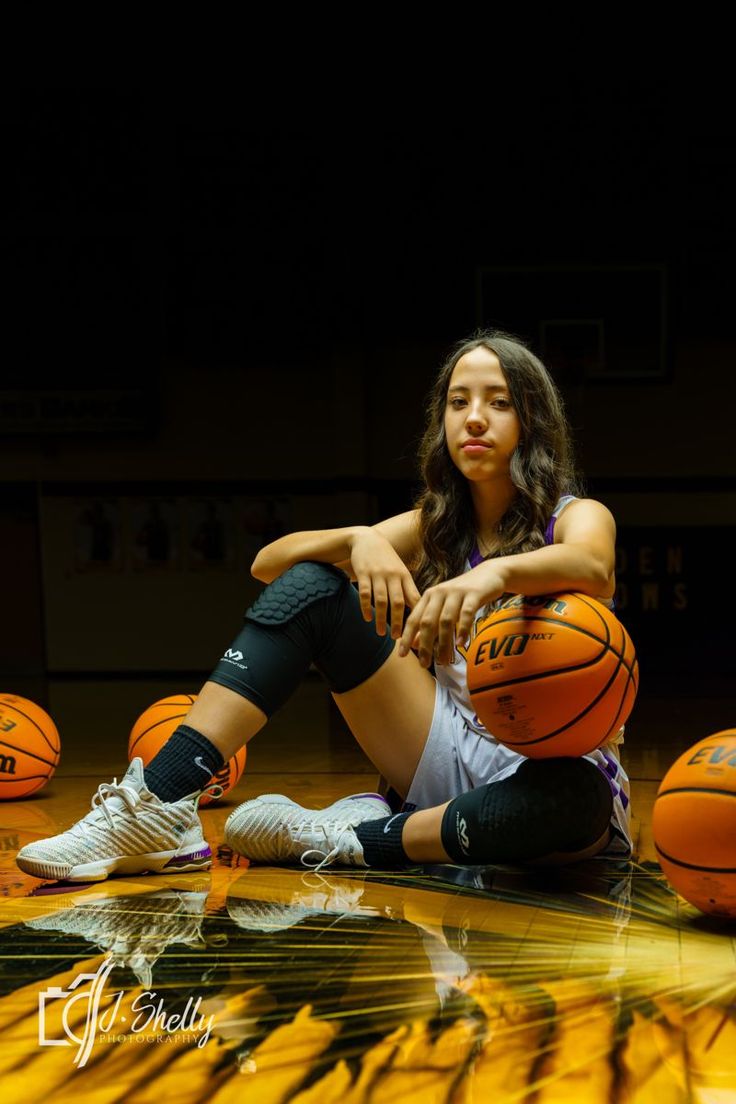 a woman sitting on the floor with basketballs around her