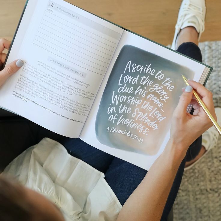 a person sitting on the floor while holding a book with writing on it and a pen in their hand