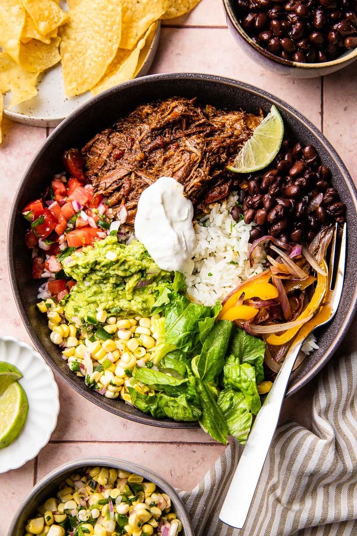 a bowl filled with mexican food next to two bowls of beans, corn and tortillas