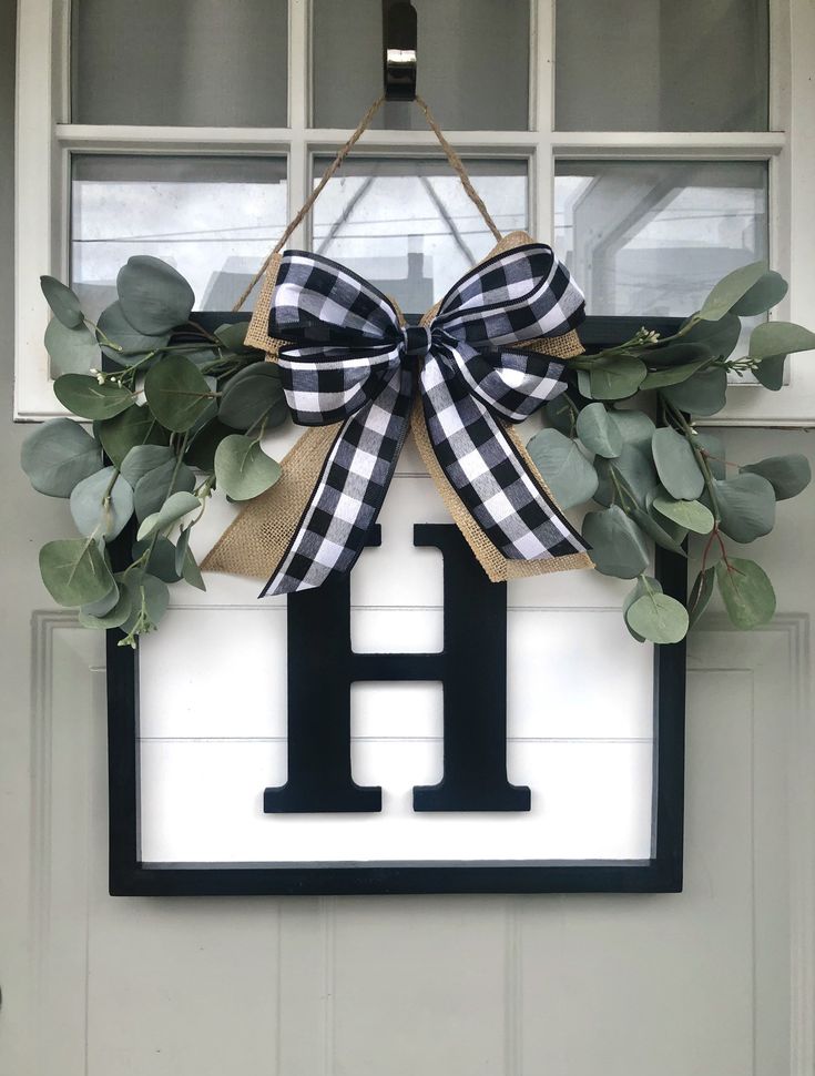 a door hanger with a monogrammed letter h and greenery on it