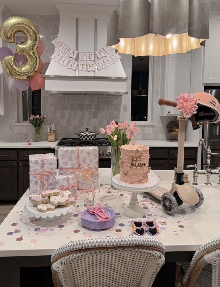 a birthday party with pink and gold decorations on the kitchen counter, balloons in the background