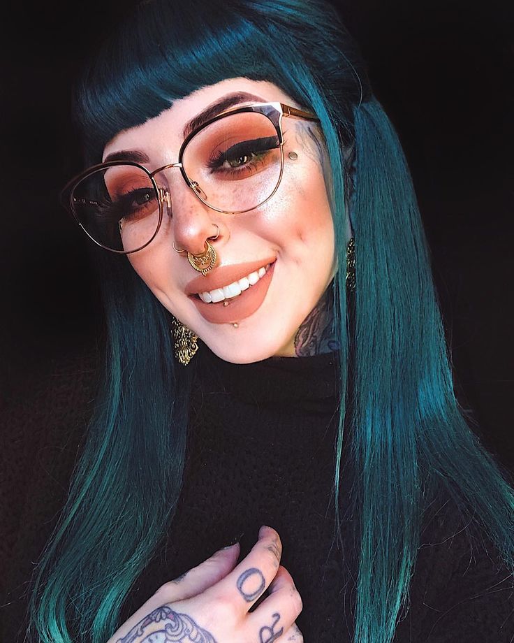 a woman with green hair wearing glasses and piercings