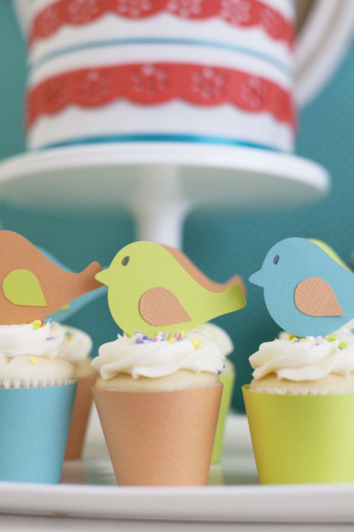 three cupcakes with paper birds on them sitting in front of a cake stand