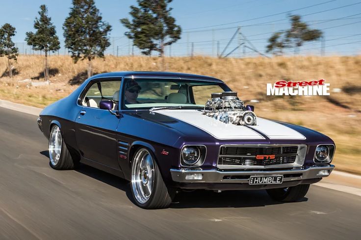 an old muscle car driving down the road with its engine on it's hood