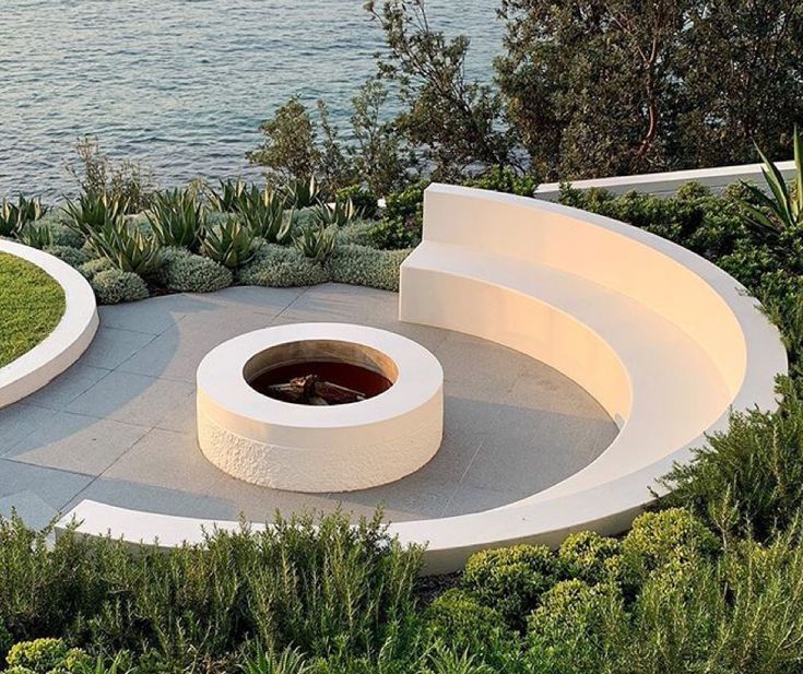 an outdoor fire pit surrounded by greenery next to the ocean