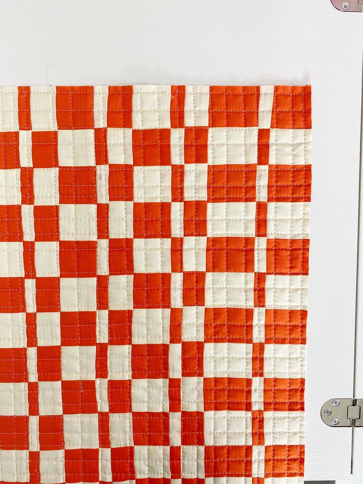 an orange and white checkered quilt hanging on the wall