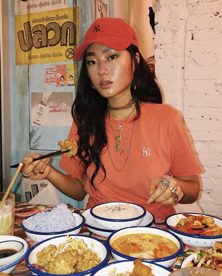 a woman sitting at a table full of food with chopsticks in her hand