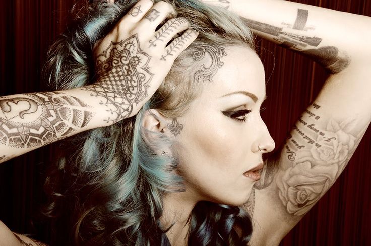 a woman with tattoos on her arms and shoulder is holding her hair in front of her head