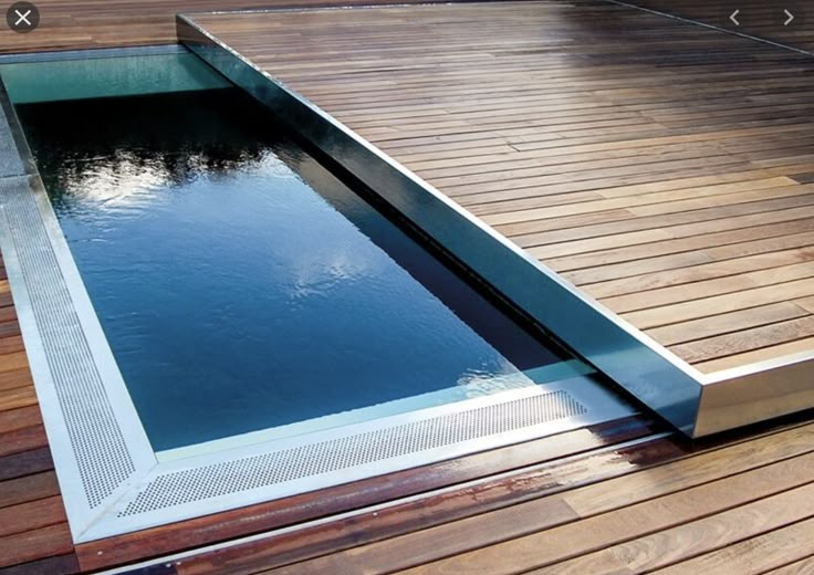 a wooden deck with a pool in the middle and sky reflected on it's surface