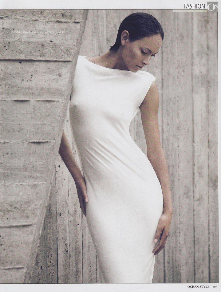 a woman in a white dress leaning against a wall