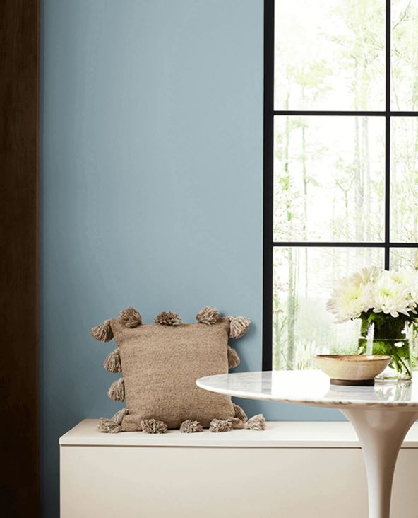 a room with blue walls, white furniture and flowers in vases on the window sill