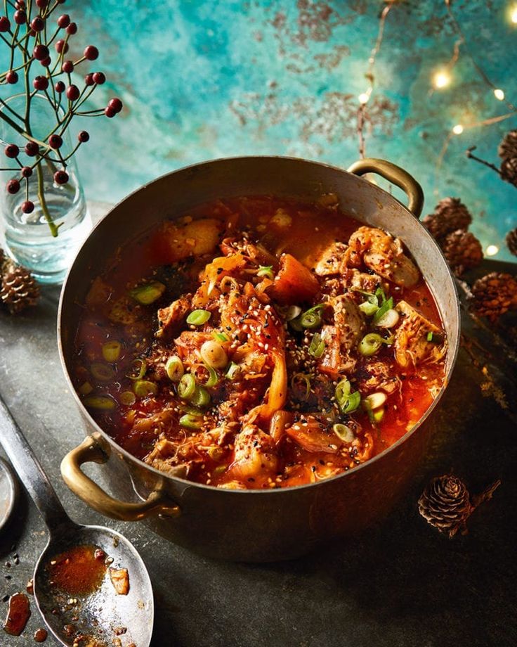 a pot filled with meat and vegetables next to spoons on top of a table