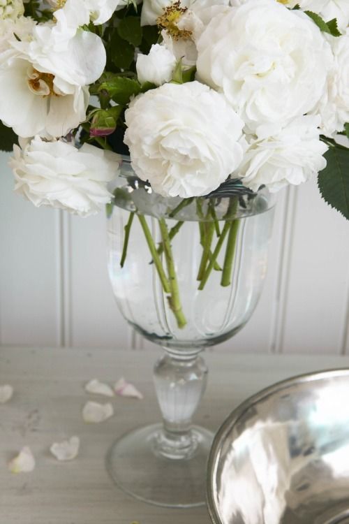 a glass vase filled with white flowers on top of a table next to a silver bowl